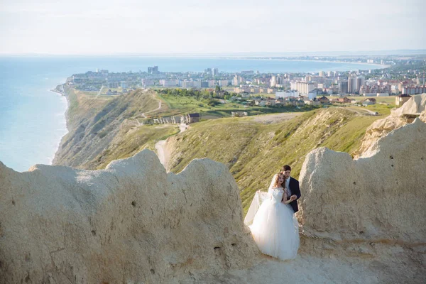 Hermosa pareja de recién casados abrazándose en el día de la boda en el acantilado con vista al mar —  Fotos de Stock