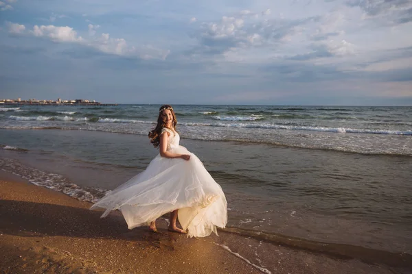 Boldog szép menyasszony, esküvői ruha fényörvények siklanak és táncok a ocean beach — Stock Fotó