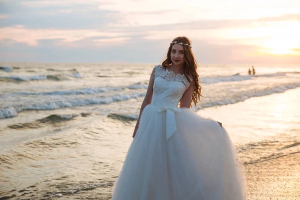 Romantikus menyasszony, fehér ruhában, óceán tengerparti strandon napnyugta időpontja. Fiatal gyönyörű menyasszony az esküvő napján — Stock Fotó