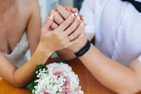Primo piano delle mani degli sposi con fedi nuziali, toccare delicatamente il bouquet di nozze di peonie . — Foto Stock