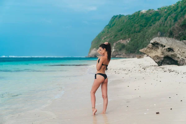 Sexy brunette meisje in een zwembroek sunbathes op het witte zandstrand. — Stockfoto