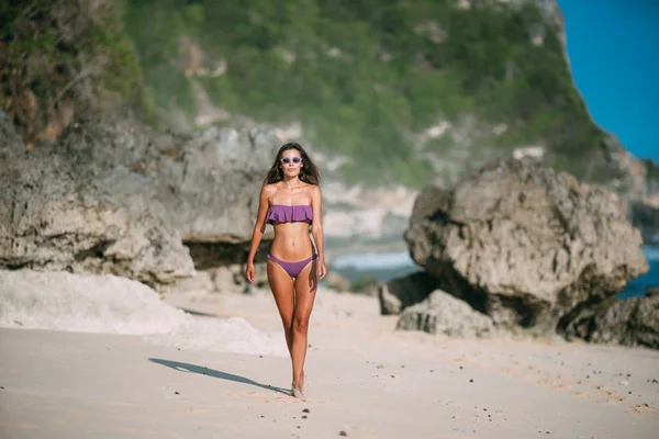 Sottile ragazza abbronzata sexy in costume da bagno in posa sulla spiaggia con sabbia e grandi pietre — Foto Stock