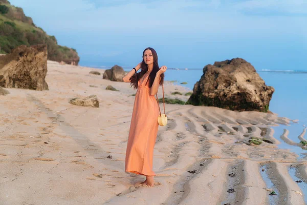 Chica atractiva en vestido de sol con bolsa en correa larga y gafas de sol posando en la playa tropical — Foto de Stock