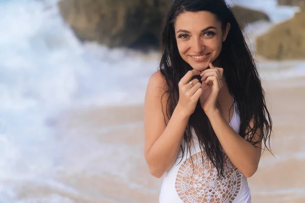 Ελκυστική ευτυχισμένος κορίτσι σε λευκό μαγιό ποζάρει στην παραλία με λευκή άμμο και μεγάλες πέτρες — Φωτογραφία Αρχείου