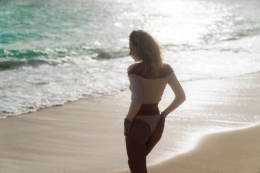 Arka görünümü bej seksi ganimet ile kızın renkli bikini ıssız sahilde dinlenme