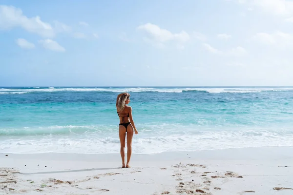 Vue arrière de la fille avec un butin sexy en bikini noir reposant sur une plage déserte — Photo