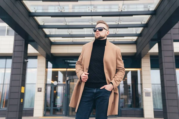 Junger bärtiger Mann mit moderner Frisur und trendigem Mantel steht in der Nähe des Business Centers — Stockfoto