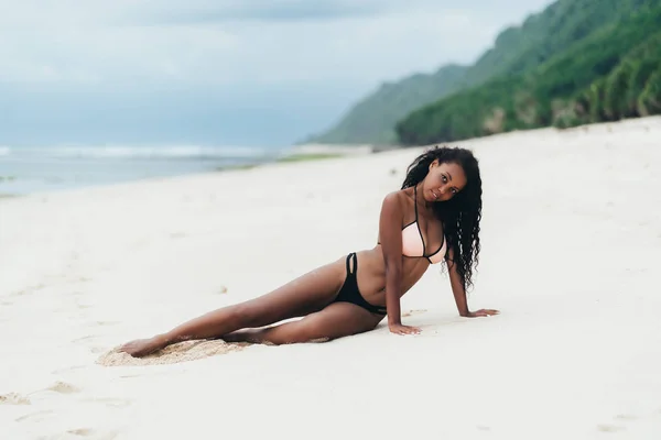 Menina afro-americana de roupa de banho deitada na praia de areia branca. Sexy modelo de pele escura com corpo perfeito repousa em feriados — Fotografia de Stock