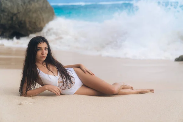 Atractiva chica feliz en traje de baño blanco posando en la playa con arena blanca y piedras grandes —  Fotos de Stock
