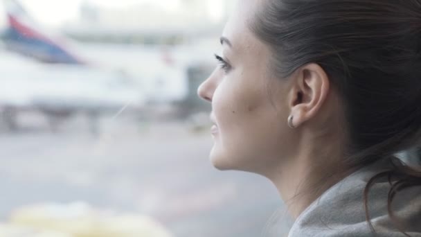 Close-up portret van mooi meisje kijkt uit raam op luchthaven op vliegtuig achtergrond — Stockvideo