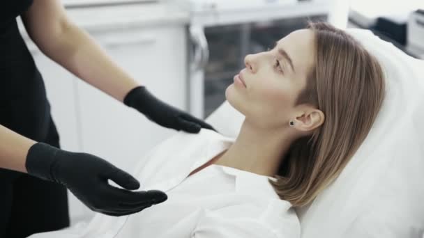 Bliska ręce kosmetyczki analizuje i dotyka twarzy pacjentów. Kobieta rozmawia z kosmetyczki przed zabiegiem — Wideo stockowe