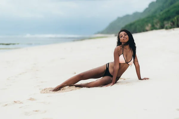 Esbelta chica sexy de piel oscura en traje de baño posando en la playa con arena. Mujer afroamericana descansando en la isla paradisíaca —  Fotos de Stock