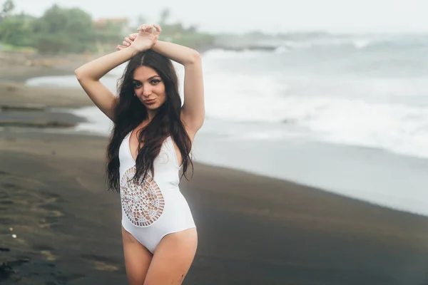 Seitenansicht von sexy Mädchen im Bikini verbringt Zeit am schwarzen Sandstrand. junge Frau mit langen Haaren posiert im Freien — Stockfoto