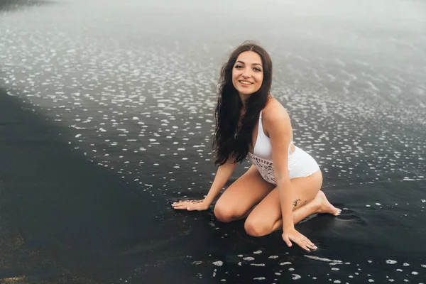 Wanita muda bahagia berbaju renang putih duduk di pantai. Girl terletak pada liburan — Stok Foto