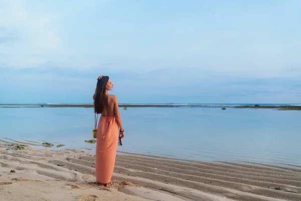 Vista trasera chica delgada con el pelo largo en vestido de sol con bolsa en largas caminatas correa en la playa tropical de arena — Foto de Stock