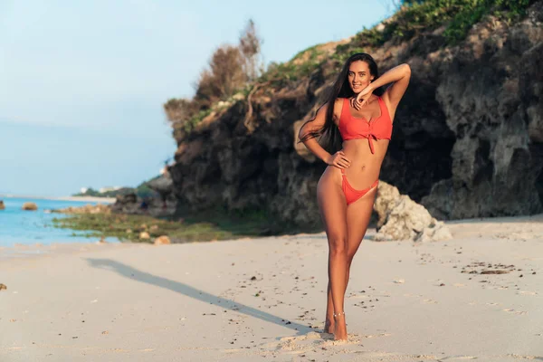 Sexy abbronzata ragazza in costume da bagno in piedi su sfondo spiaggia di grandi pietre — Foto Stock