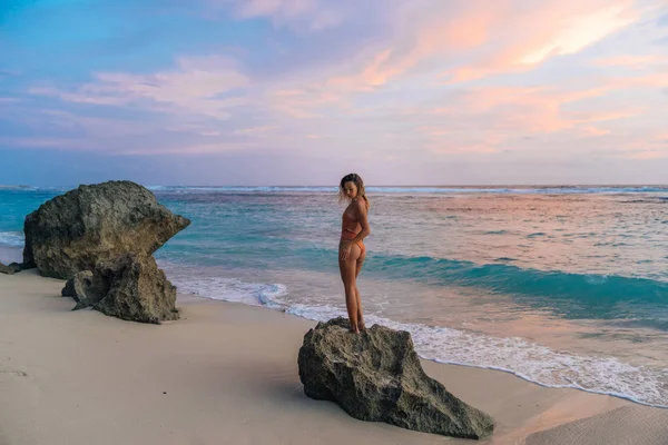 Rückseite Mädchen im Bikini steht am Strand im Hintergrund des Sonnenuntergangs mit schöner Farbe des Himmels — Stockfoto