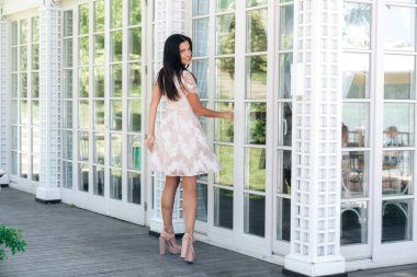 Şirin esmer güzel uzun bacaklar dışında bej renk elbise yakınındaki bir ahşap ve cam duvar poz ile