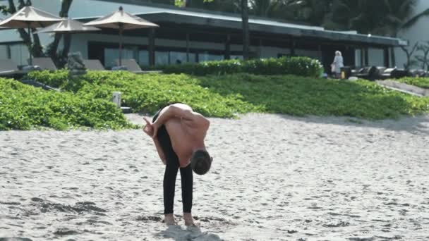 Hombre atlético haciendo ejercicios de pose de yoga y pilates en la playa de arena — Vídeos de Stock