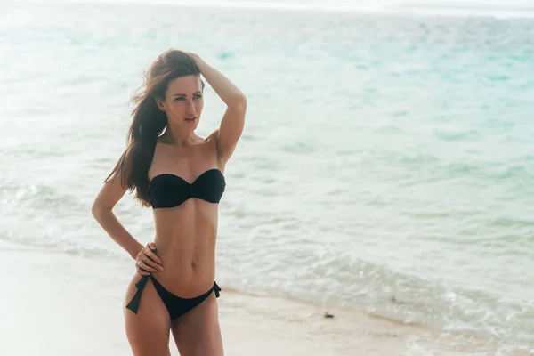 Modelo bronceado sexy en traje de baño negro posando en la playa de arena blanca —  Fotos de Stock
