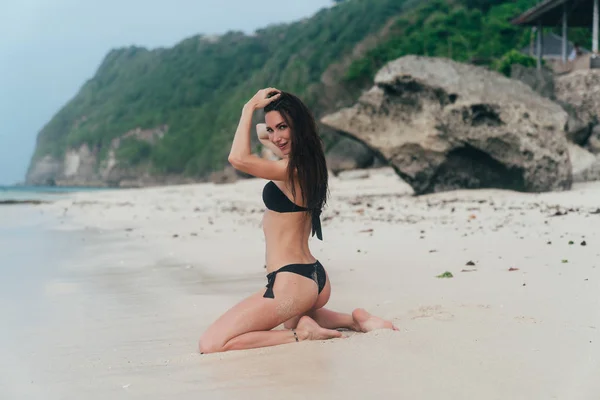 Красива модель в чорному купальнику позує на білому піщаному пляжі — стокове фото