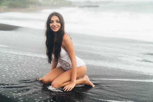 Mujer joven y feliz en traje de baño blanco se sienta en la playa del océano. Chica descansa de vacaciones —  Fotos de Stock