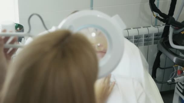 Крупним планом косметолог вивчає область навколо губ пацієнта через косметичне збільшувальне скло — стокове відео