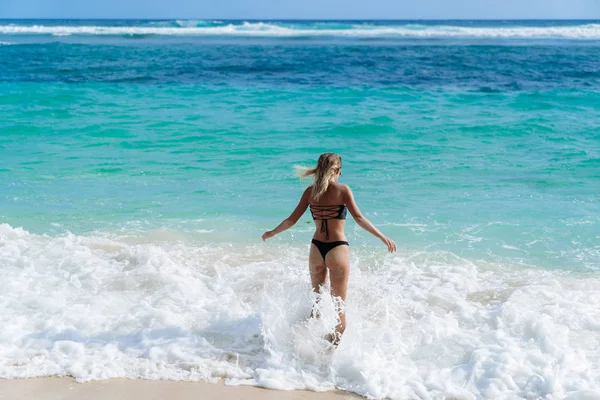 Slim sexy chica en traje de baño negro va a nadar en el océano en la playa — Foto de Stock