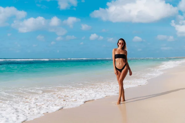 Sexy gelooid meisje in een zwarte zwembroek en de zonnebril gaat op tropisch strand — Stockfoto