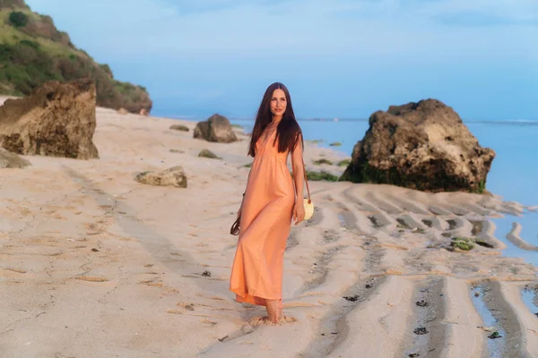 Chica atractiva en vestido de sol con bolsa en correa larga y gafas de sol posando en la playa tropical — Foto de Stock