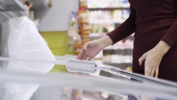 Vrouw opent koelkast, bevroren voedsel zoekt en sluit het in supermarkt — Stockvideo