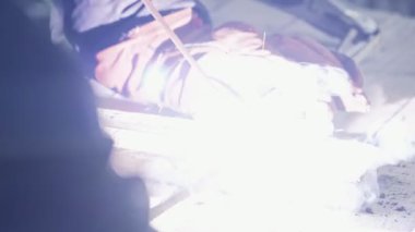 Yan görünümü Kaynakçı Kaynak maskeli iki metal parçalar kaynak. İşçi tulumu içinde kapalı çalışıyor