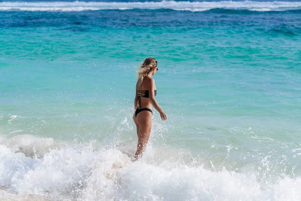 Slim sexy chica en traje de baño negro va a nadar en el océano en la playa — Foto de Stock