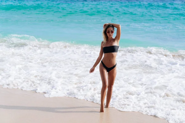 Menina bonita em maiô preto e óculos de sol descansando perto do oceano na praia — Fotografia de Stock