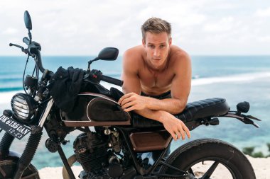 Arka planda okyanus ile özel motosiklet üzerinde çıplak gövde ile seksi atletik adam portre