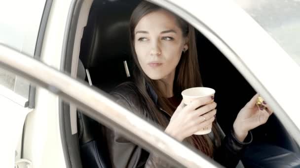 Bella ragazza si siede sul sedile anteriore in auto e beve caffè . — Video Stock