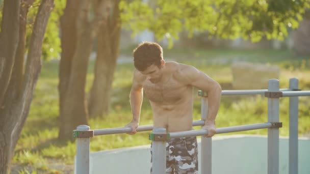 Fitness man training on uneven bars on summer sport ground — Stock Video