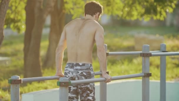 Vista trasera del hombre de fitness haciendo ejercicios en las barras en el campo atlético — Vídeo de stock