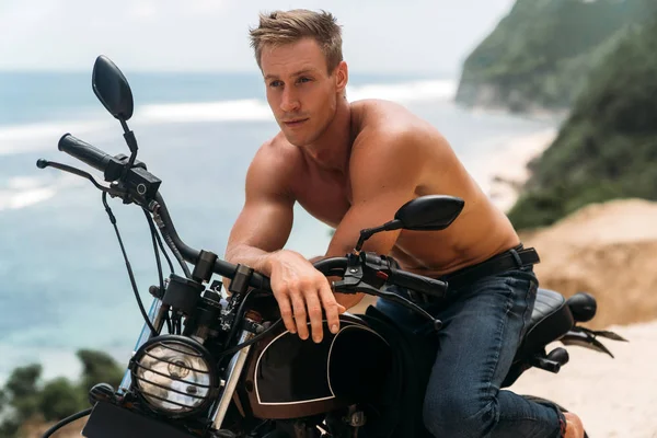 Arka planda okyanus ile özel motosiklet üzerinde çıplak gövde ile seksi atletik adam portre