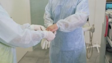 Hemşire hastanede skleroterapi ameliyatı öncesinde steril eldiven koymak için bir cerrah yardımcı olur