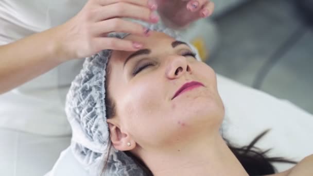 Nahaufnahme der Hände eines Kosmetikers im Schönheitssalon, der einer Frau mit geschlossenen Augen eine Gesichtsmassage anbietet. — Stockvideo