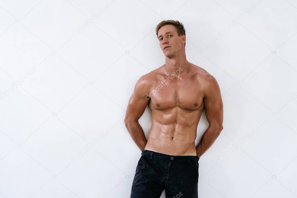 Handsome man in athletic uniform on white background. Fitness model posing in black pants