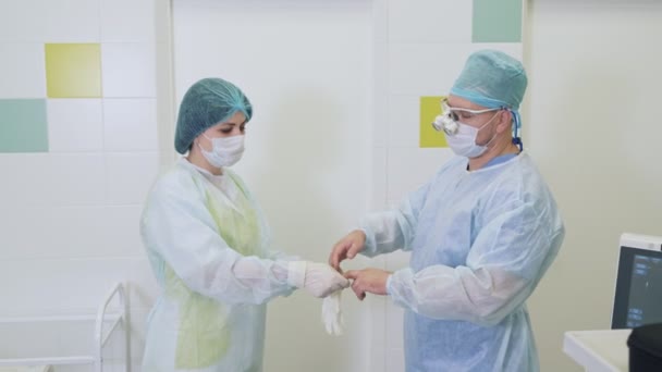 Infermiera aiuta un chirurgo a indossare guanti sterili prima di un intervento di scleroterapia in ospedale — Video Stock