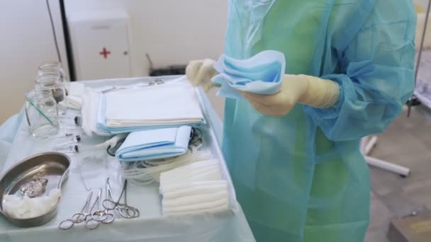 Enfermeira em roupas e luvas estéreis prepara instrumentos e cobertura médica cirúrgica antes da cirurgia — Vídeo de Stock
