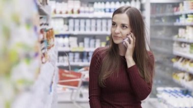 Güzel kız gülümseyerek, telefonda konuşurken ve süpermarkette alışveriş