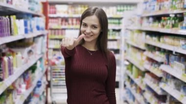 Süpermarkette başparmak yukarı gösteren geniş gülümseme ile güzel genç kadın