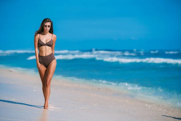 Sexy modello abbronzato con occhiali da sole in costume da bagno marrone in posa sulla spiaggia di sabbia bianca — Foto Stock