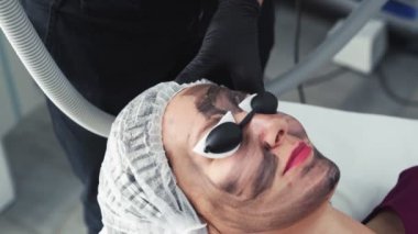 Yakın eller güzellik kliniğinde genç kadının yüzünde karbon peeling işlemi yapar