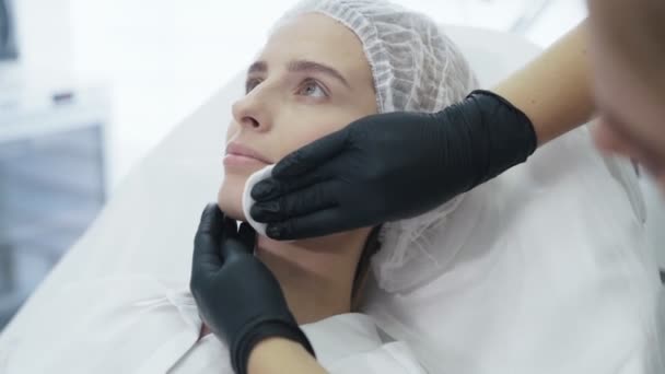 O close-up lento das mãos dos médicos desinfecta e limpa o rosto dos pacientes com disco de algodão antes do tratamento — Vídeo de Stock