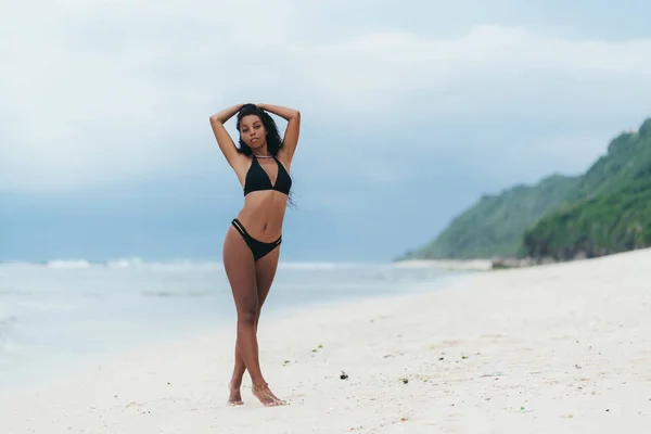 Esbelta chica sexy de piel oscura en traje de baño posando en la playa con arena. Mujer afroamericana descansando en la isla paradisíaca —  Fotos de Stock